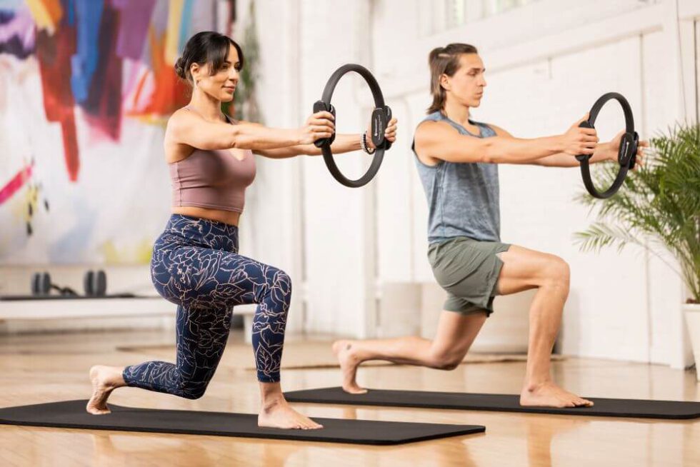 Divi cilvēki veic izklupienus ar Ultra-Fit apli studijā.