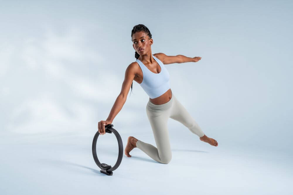 Sieviete demonstrē Pilates vingrinājumu ar Ultra-Fit apli.