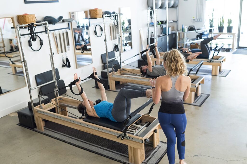 Pilates nodarbība, izmantojot klīniskos reformerus ar torni studijā.