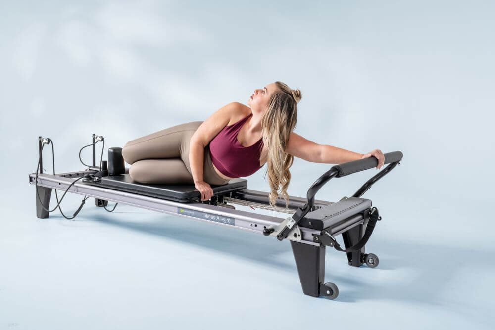 Sieviete veic Pilates vingrinājumu uz Allegro Reformer no Balanced Body.