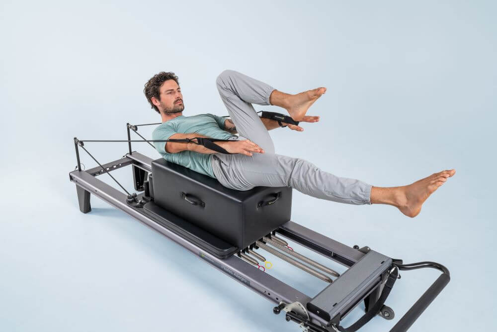 Persona demonstrē vingrinājumu uz Allegro Reformer Pilates trenažiera.