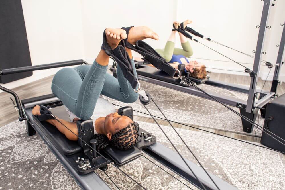 Два человека используют Allegro Reformer Konnector в студии пилатеса.