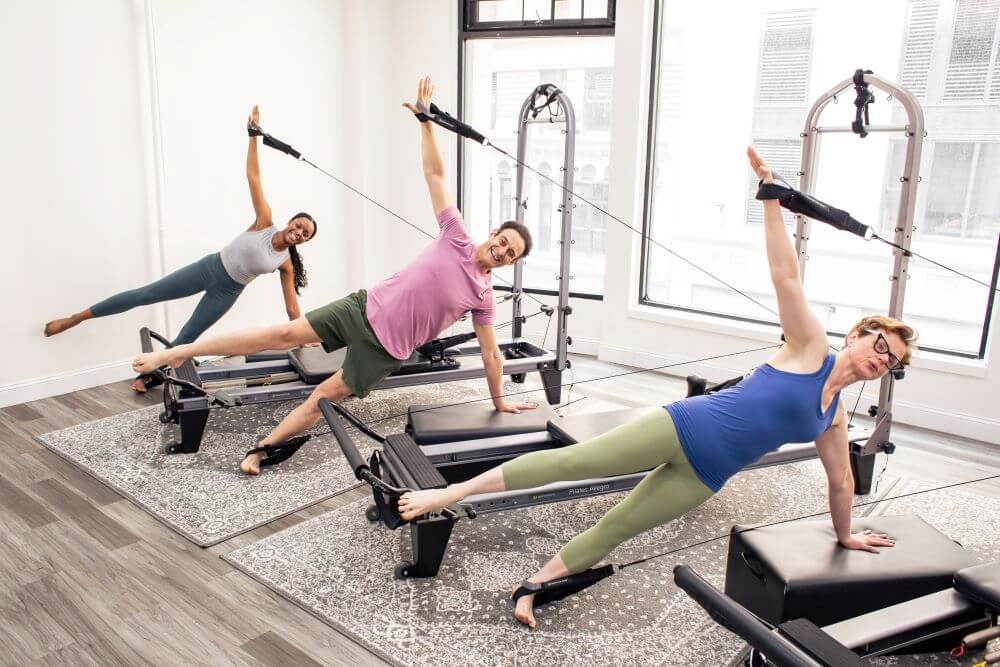 Люди занимаются на тренажёре Allegro Reformer Konnector в студии.