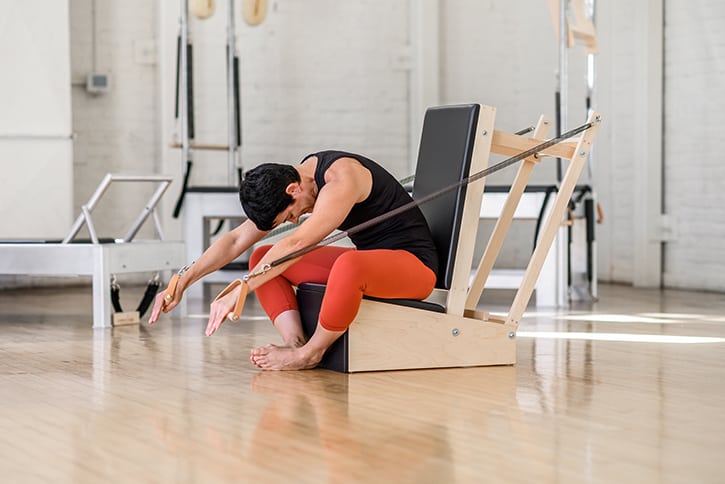 Instruktors demonstrē vingrinājumu uz Contrology roku krēsla studijā.