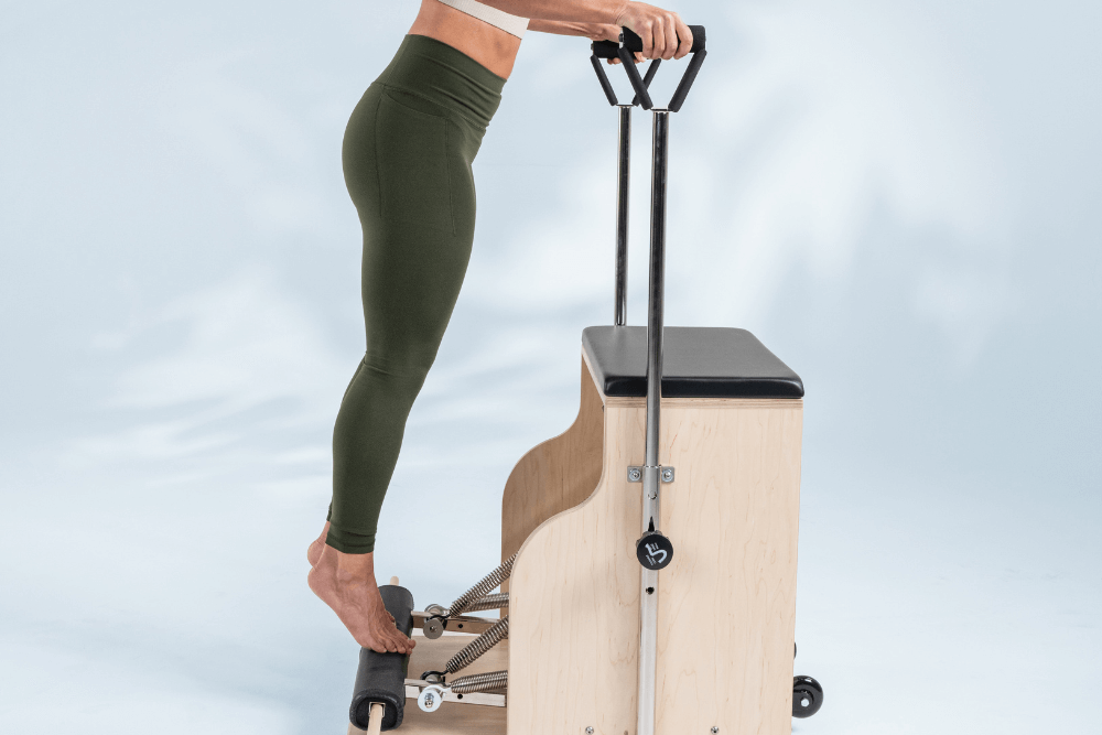 Pilates kombinētais krēsls ar lietotāju, kurš stāv un turas pie rokturiem.