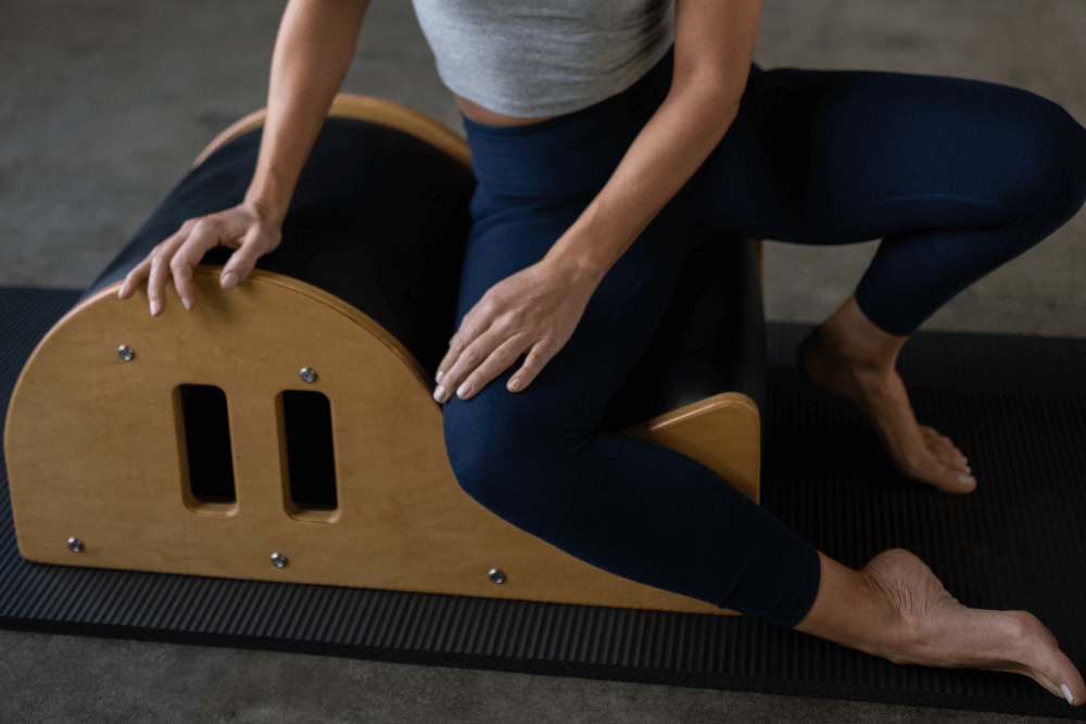 Persona izmanto Clara Step Barrel Pilates vingrinājumam uz paklājiņa.