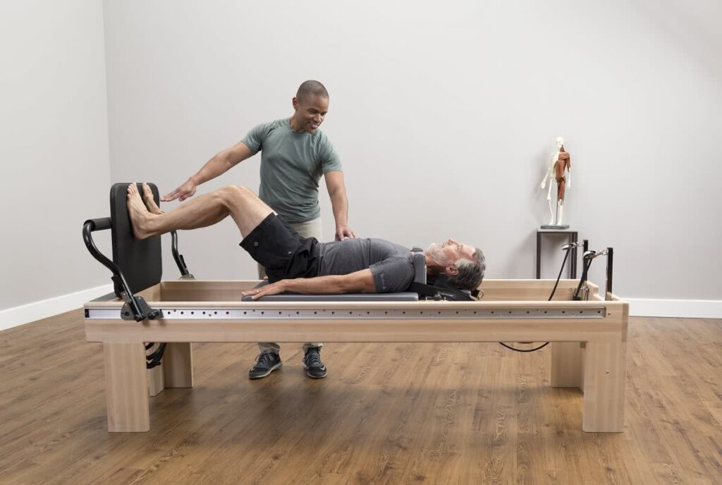 Instruktors asistē vīrietim uz Clinical Reformer Pilates trenažiera.