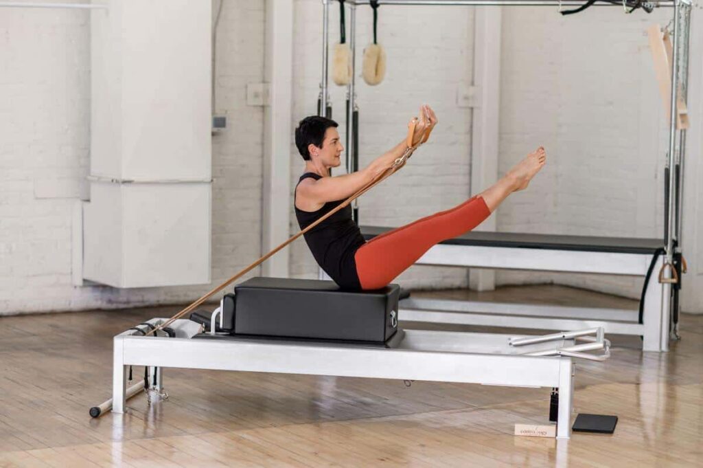 Persona veic Pilates vingrinājumu sēdus pozīcijā uz Contrology kastes.