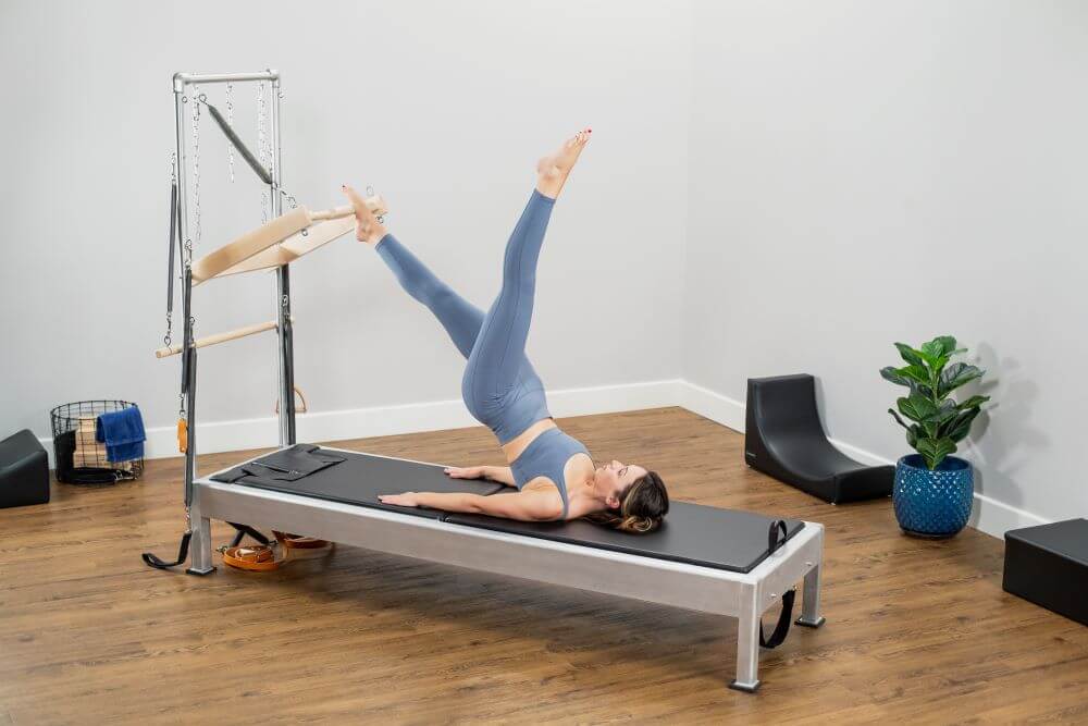 Sieviete vingro uz Contrology Reformer ar torni un vingrošanas paklājiņu.