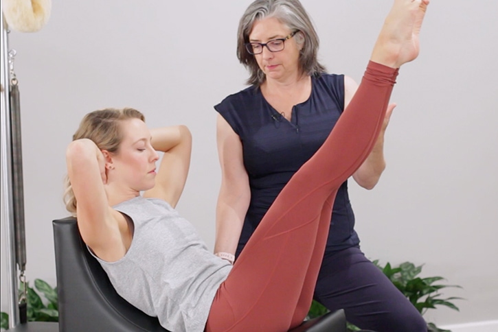 Instruktors palīdz ar Pilates vingrinājumu uz C-Shaper ierīces.