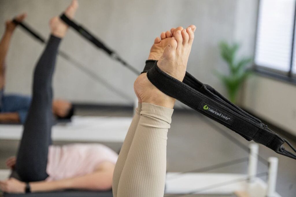 Человек использует двойные петли Balanced Body на реформере для пилатеса.