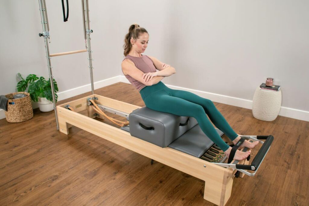 Тренажёр реформер для пилатеса с сиденьем и ножными ремнями в использовании.