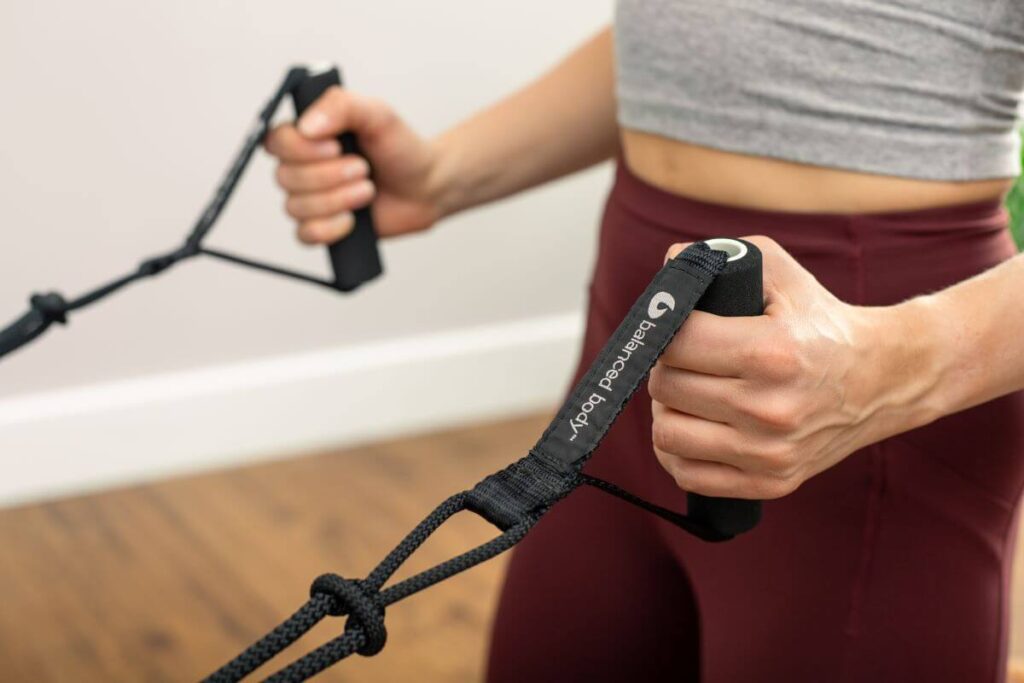 Крупный план рук, держащих неопреновые ручки Balanced Body для пилатеса.