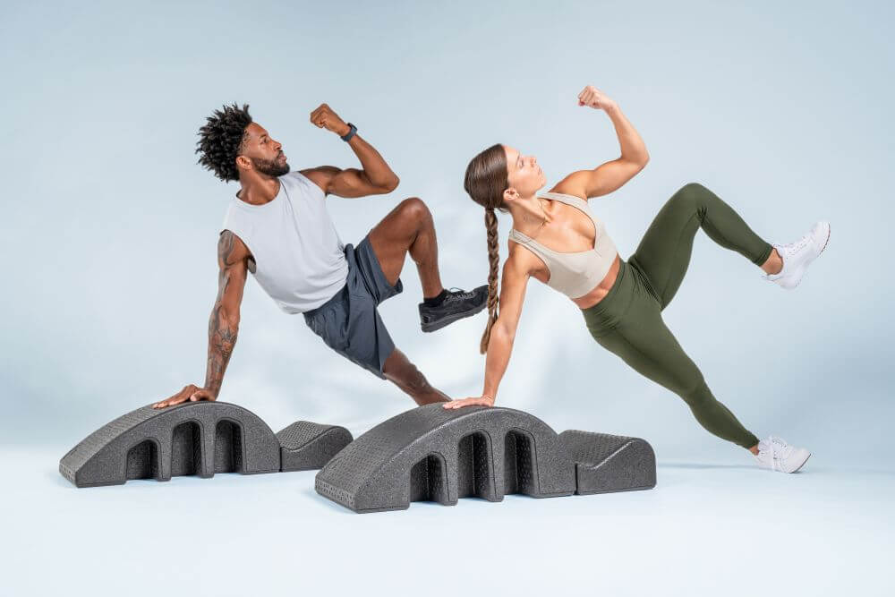 Два человека выполняют упражнения на тренажёре Pilates Arc для укрепления мышц кора.