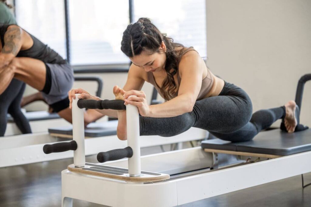 Persona izmanto Allegro 2 Reformer dēļa stieņus Pilates vingrinājumam.