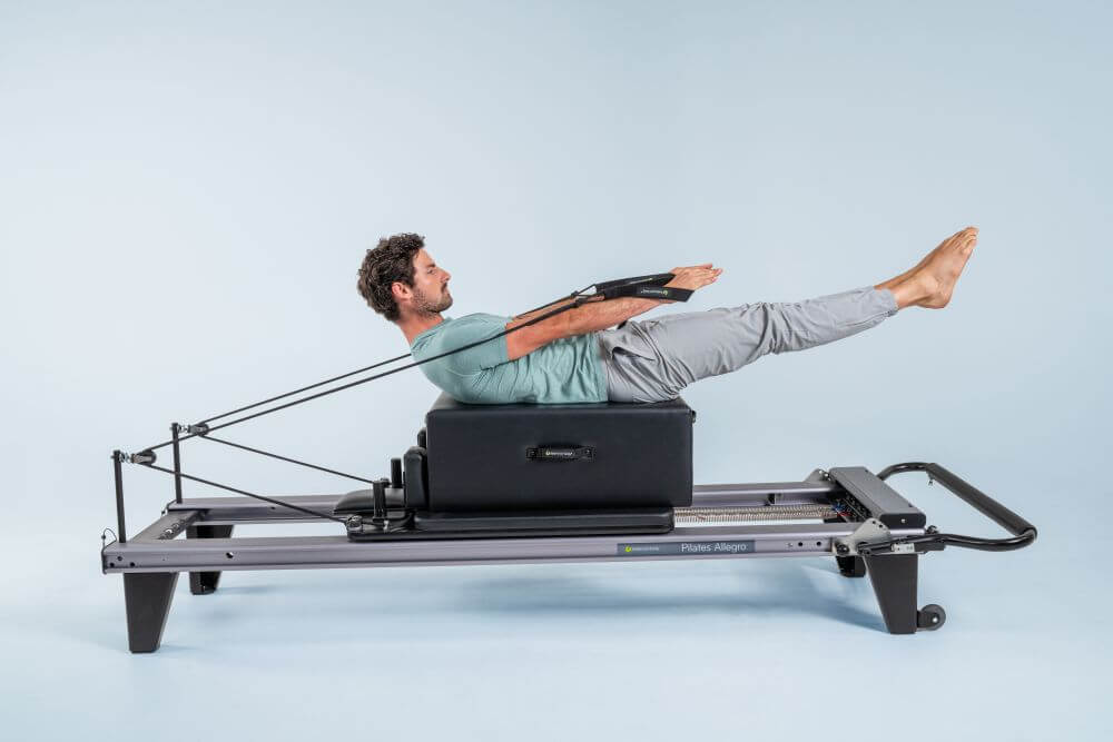 Vīrietis vingro ar Allegro Reformer Pilates aprīkojumu studijā.