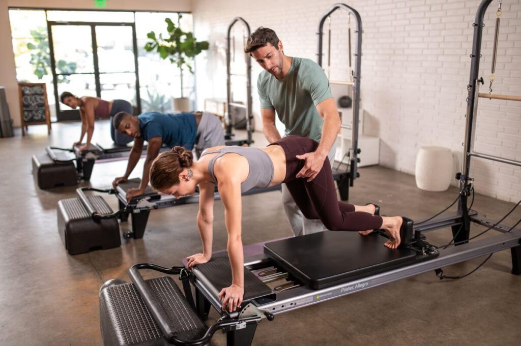 Pilates instruktors palīdz uz Allegro Reformer ar platformas pagarinātāju.
