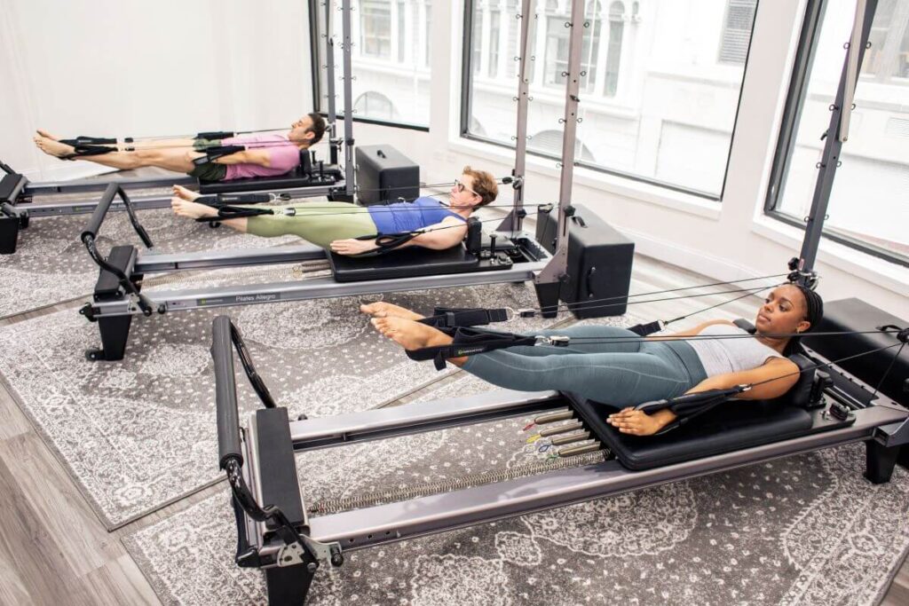 Trīs cilvēki izmanto Pilates trenažierus ar Signature atsperēm.