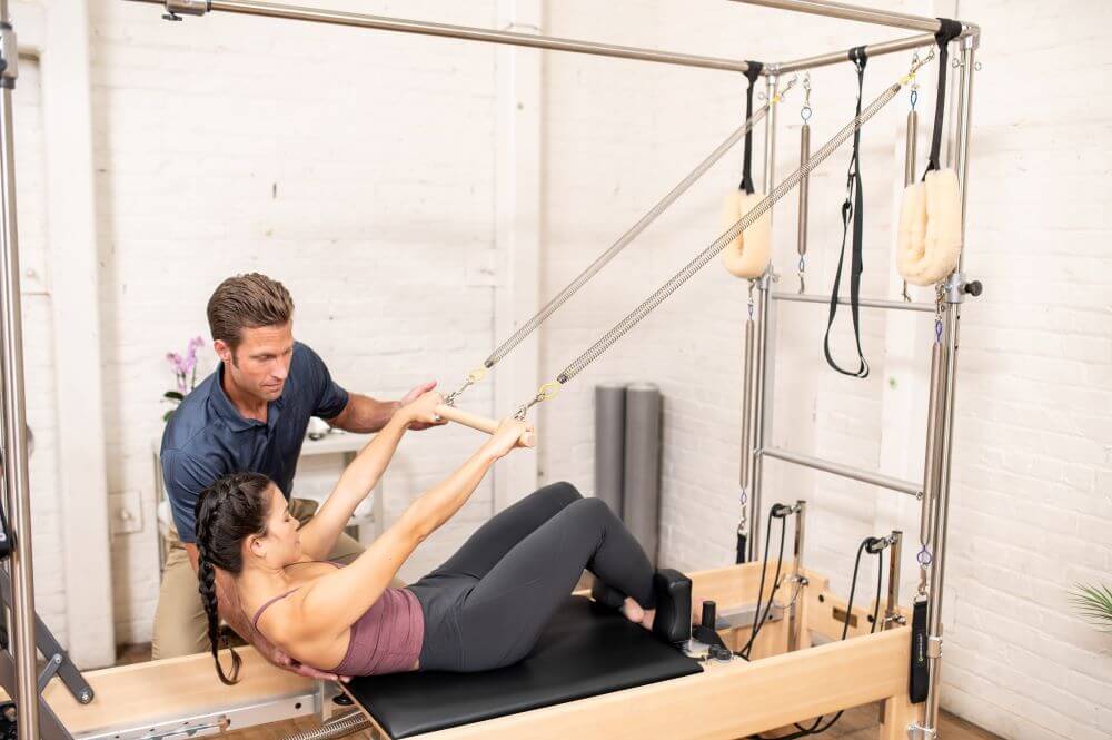 Instruktors palīdz klientam uz Reformer Trapeze kombinācijas trenažiera.