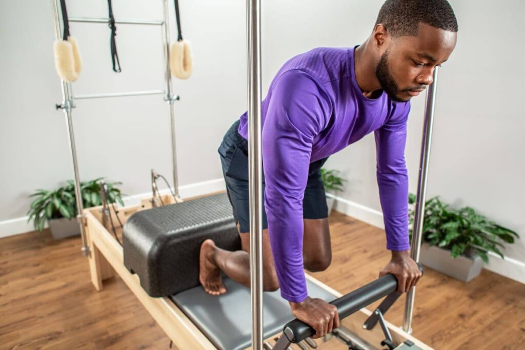 Vīrietis izmanto Sitting Box Lite uz Pilates trenažiera