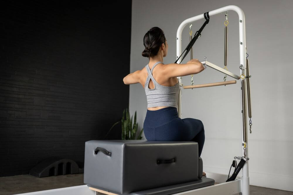 Sieviete izmanto standarta sēdēšanas kasti uz Pilates trenažiera vingrošanai.