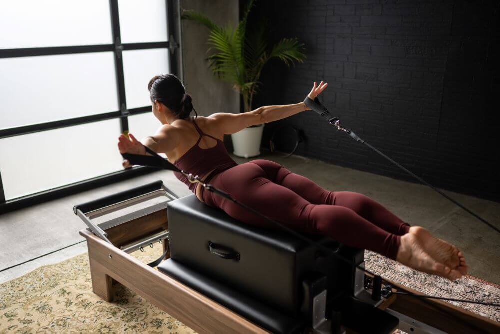 Persona veic pilates vingrinājumus uz reformera ar standarta sēdēšanas kasti.