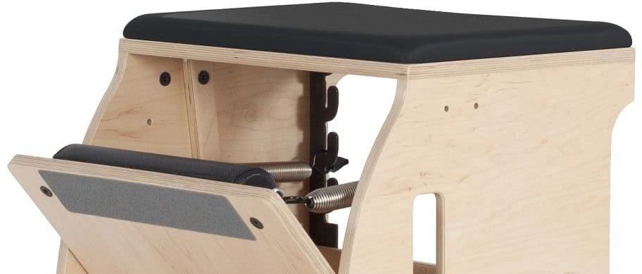 Pilates aprīkojums ar koka rāmi un melnu polsterētu sēdekli.