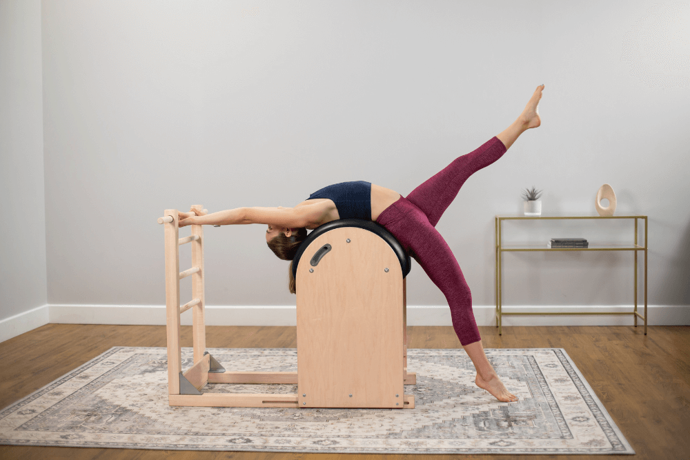 Sieviete izstiepjas uz Balanced Body kāpņu mucas, veicot Pilates vingrinājumus.