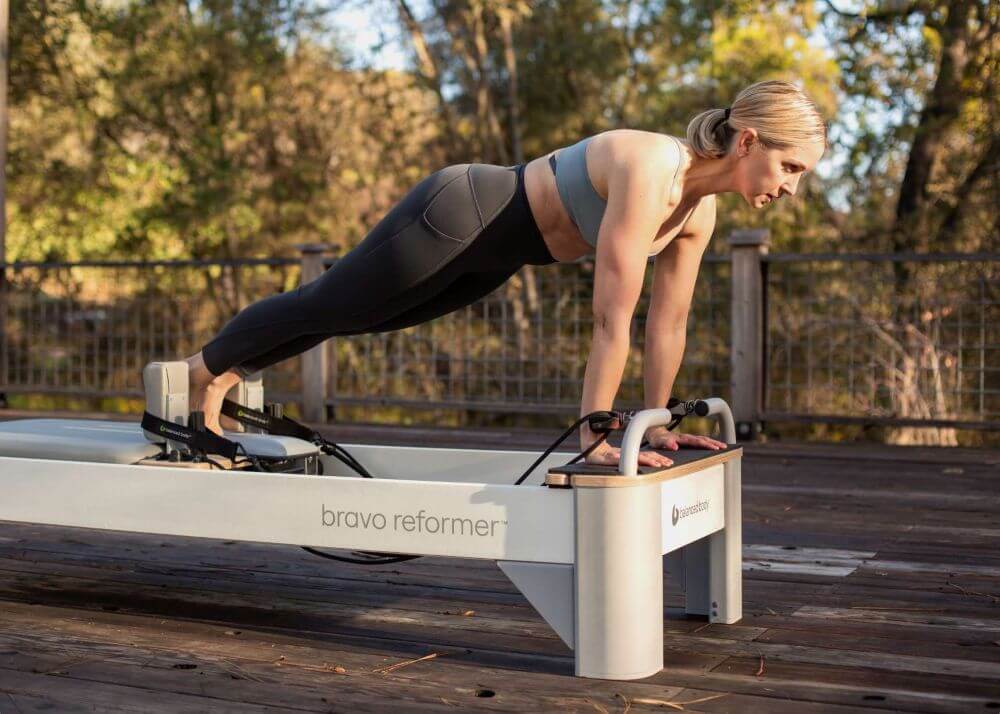 Человек занимается на Bravo Reformer с удлинённой передней платформой на открытом воздухе.