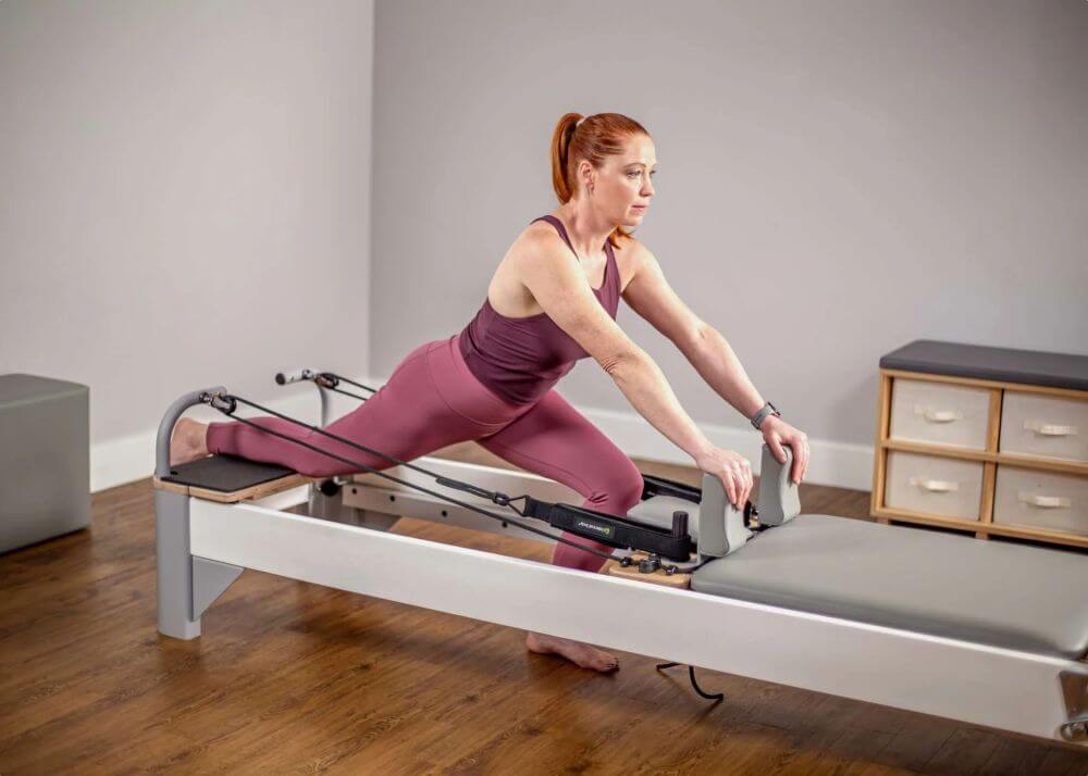 Женщина выполняет растяжку на платформе Bravo Reformer Extended Head End.