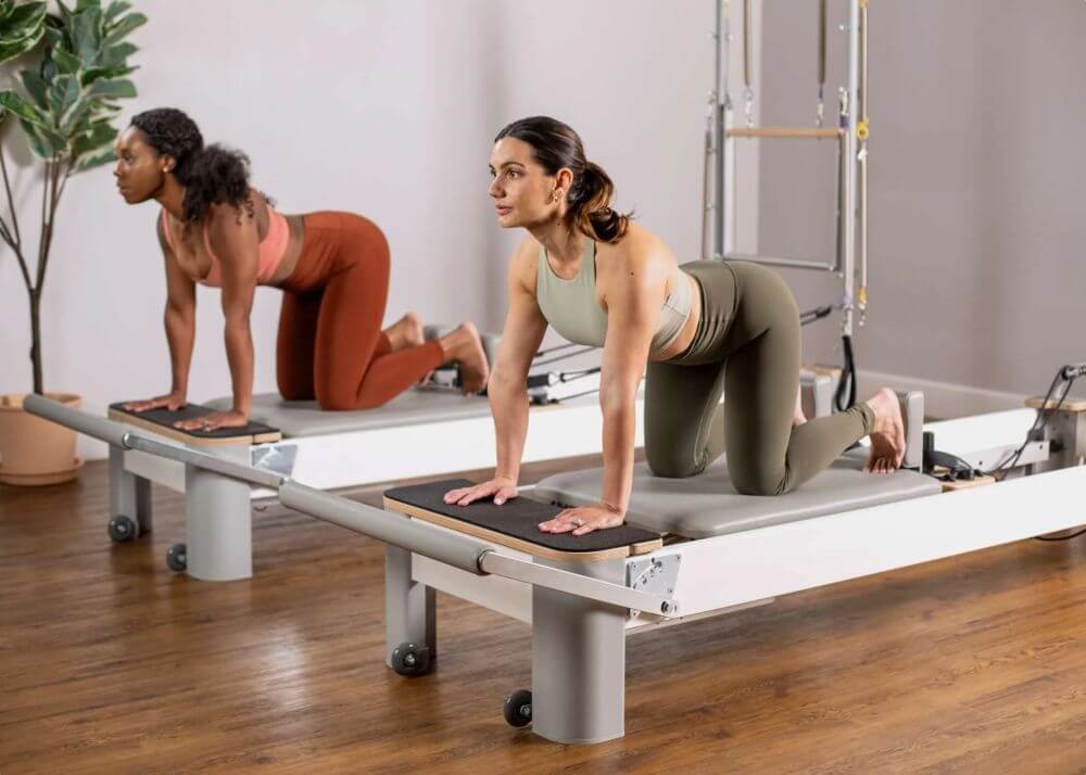 Divas sievietes vingro uz Bravo Reformer Platform Extender paplašinājumiem.