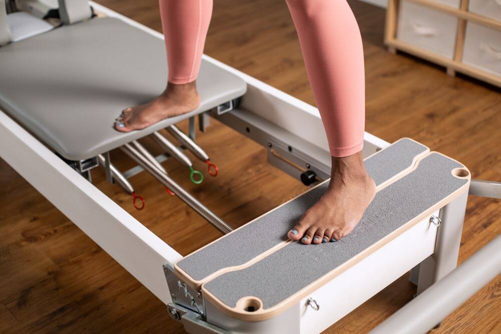 Bravo Reformer Platform Extender ar kājām, demonstrējot lietošanu.